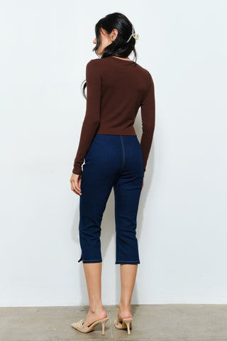 Woman wearing a brown long-sleeve top and blue jeans against a white background