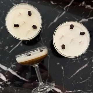 Three espresso martini candles presented on a marble surface, with the candle in the foreground partially melted, revealing coffee beans embedded in the wax.
