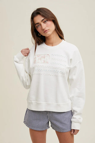 Model wearing a white floral American flag pullover sweatshirt with blue striped shorts, shown from the front against a neutral background.