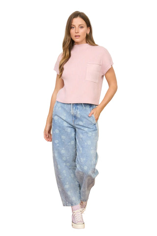 Woman wearing a pink top and light blue jeans standing in front of a green couch.