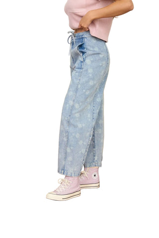 Person wearing light blue jeans and pink shoes standing in a room with a yellow couch.