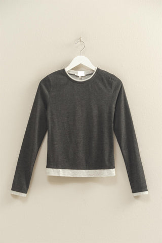 Dark gray long-sleeve shirt on a hanger against a beige wall