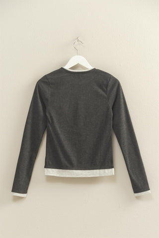 Dark gray long-sleeve shirt on a hanger against a beige wall
