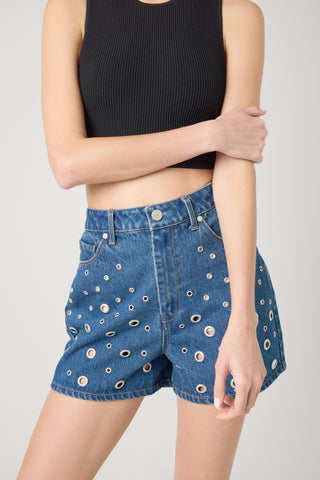 A pair of high-waisted denim shorts with metallic grommets and a button-fly closure.