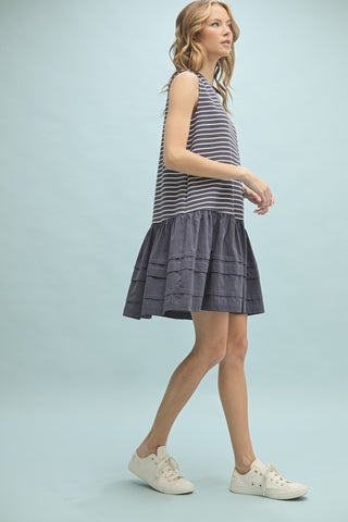 Side view of model walking in navy and white striped drop waist dress with ruffle hem