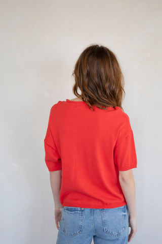 woman wearing red vest cardigan and jeans. back view on a white backdrop. 