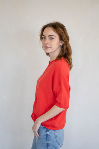 woman wearing red vest cardigan with jeans. side view against a white background.