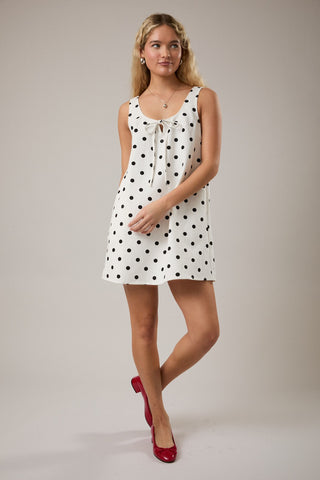 Woman wearing a white dress with black polka dots against a plain background