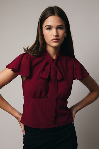 Woman wearing a burgundy blouse with ruffled shoulders against a neutral background