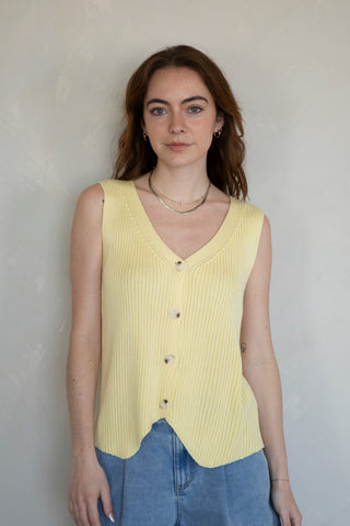 woman wearing butter yellow knit vest with shorts. front view against white background. 