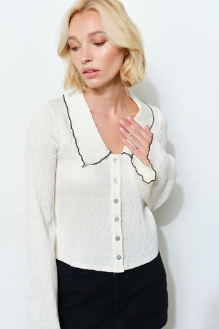 Woman wearing a white blouse with black trim against a plain background