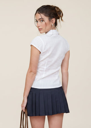 Woman wearing a white short-sleeve shirt and navy pleated skirt against a red background